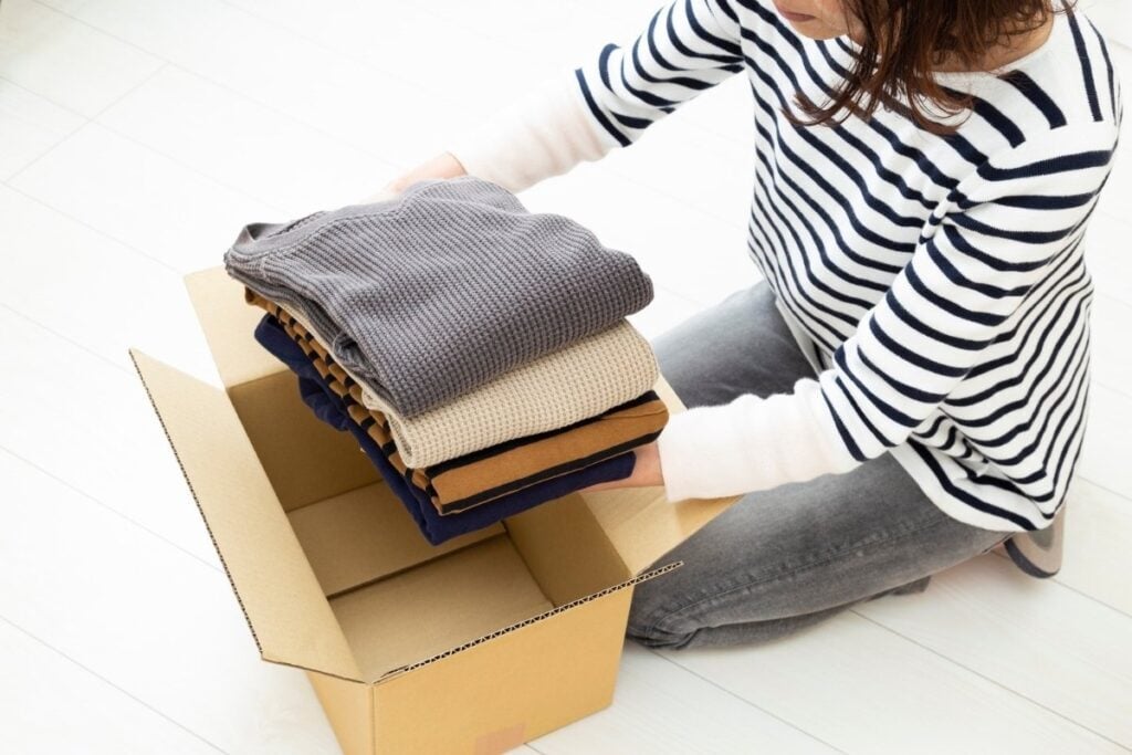 Packing folded clothes into a cardboard box.