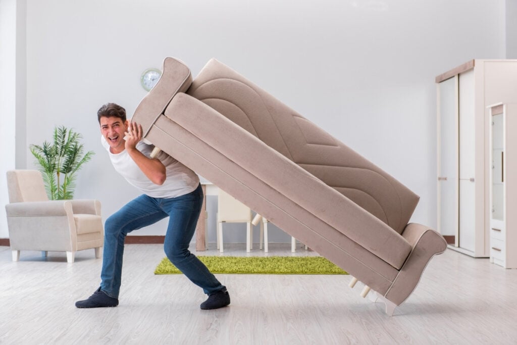 Man struggling to carry a heavy sofa alone.